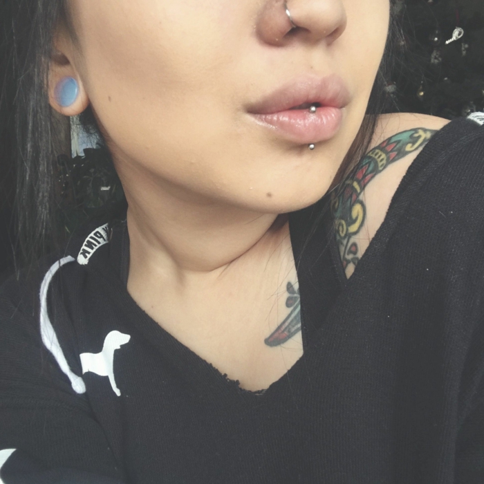 girl wearing black blouse, horizontal lip piercing, lips with clear lip gloss, nose ring piercing