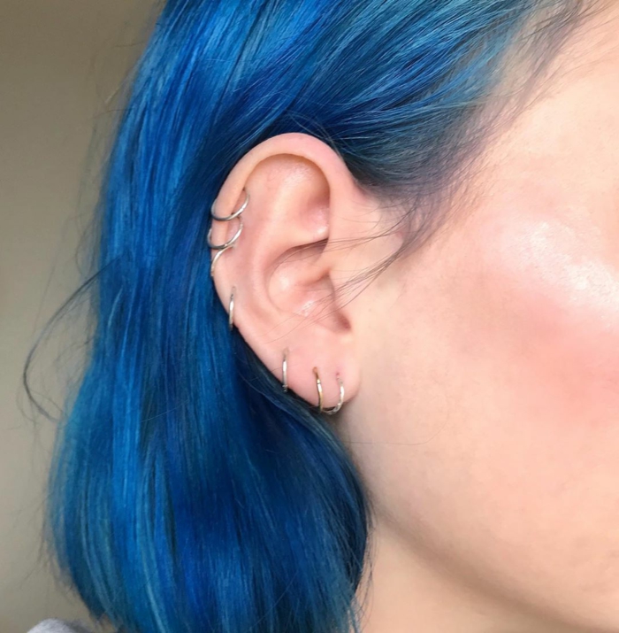 close up photo of an ear, hoop cartilage piercing, woman with blue hair, wearing silver ring earrings