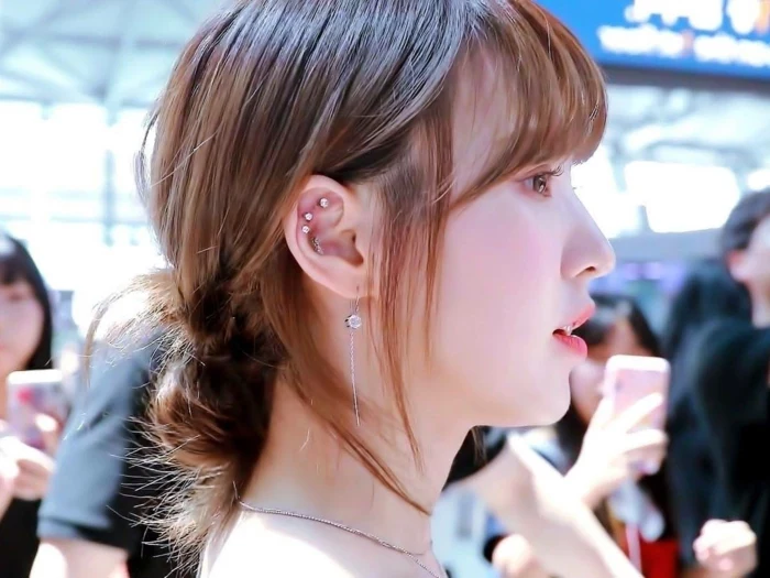 woman with brown hair in a low updo, wearing multiple earrings with rhinestones, hoop cartilage piercing