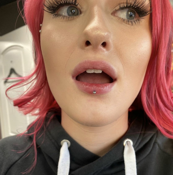types of lip piercings, woman with pink hair and green eyes, long eyelashes and clear lip gloss