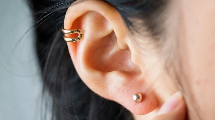 close up photo of an ear, hoop cartilage piercing, woman with black hair, gold ring earrings