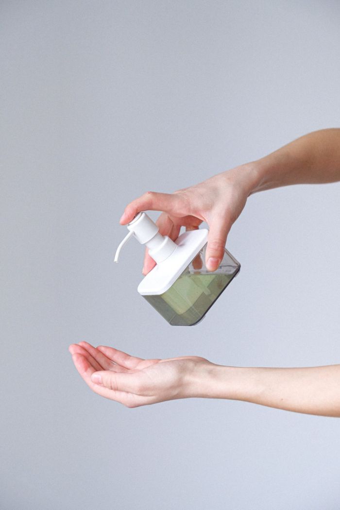 plastic bottle full of antibacterial gel, hand sanitizer, sprayed on female hand, white background