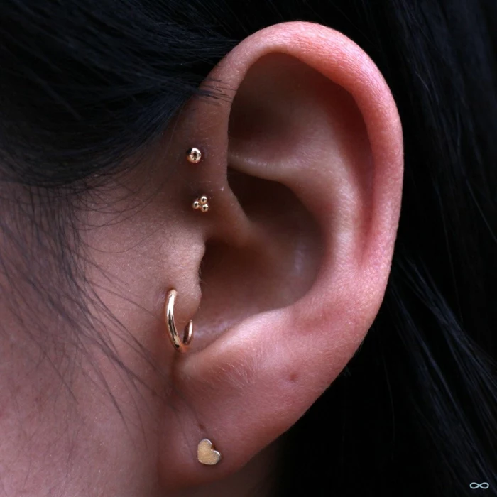 cartilage piercing earrings, close up photo of an ear, woman with black hair, wearing multiple stud earrings