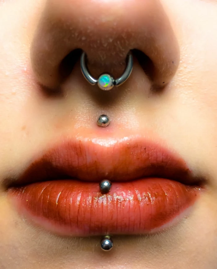 septum ring piercing with blue rhinestone, different lip piercings, close up photo, lips with red lip gloss
