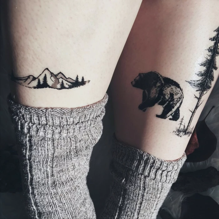 leg tattoos, mountain range on one leg, bear and tall tree on the other, mountain tattoo, grey socks
