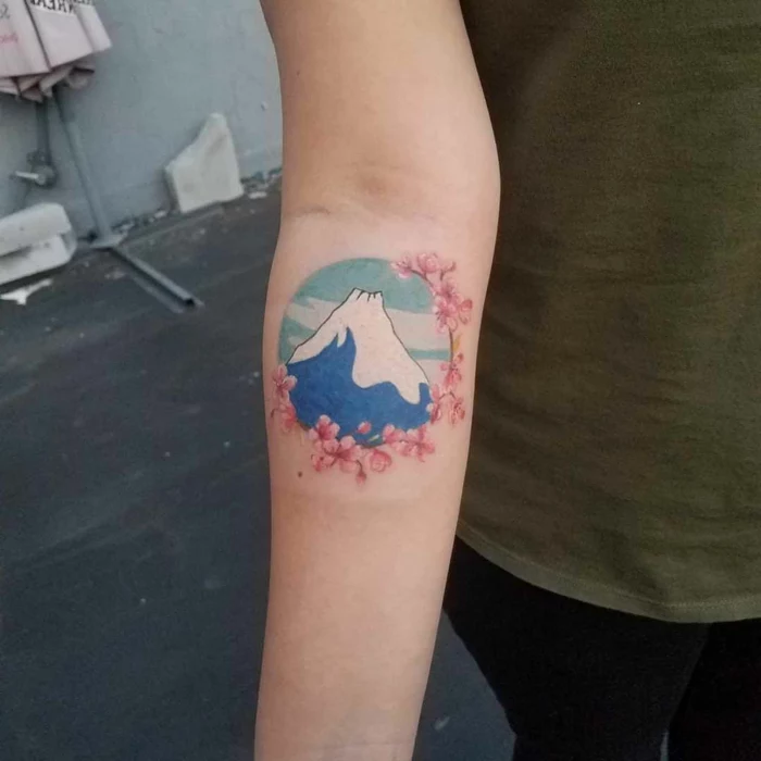 mountain with snowy peak, blue sky inside a circle, surrounded by cherry blossoms, mountain tattoo ideas, watercolor forearm tattoo