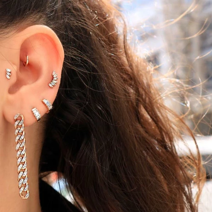 woman with brown wavy hair, wearing multiple earrings with rhinestones, stud cartilage piercing