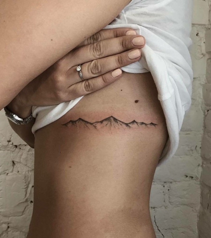 mountain scene tattoo, rib cage tattoo, minimalist mountain range, woman wearing white top