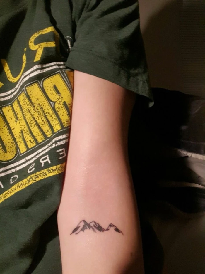 mountain tattoo meaning, forearm tattoo, minimalist mountain range, woman wearing black t shirt