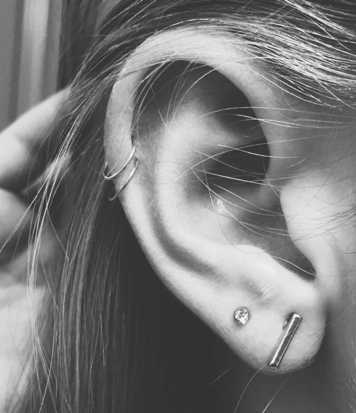 black and white photo, how much is a cartilage piercing, close up photo of an ear, multiple earrings