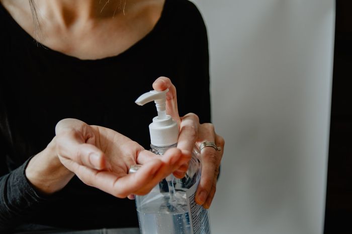 woman spraying antibacterial gel on her hand, wearing black blouse, hand sanitizer