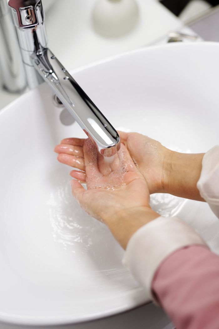 woman wearing pink blouse, washing hadn under running water, hand sanitizer ingredients, white sink