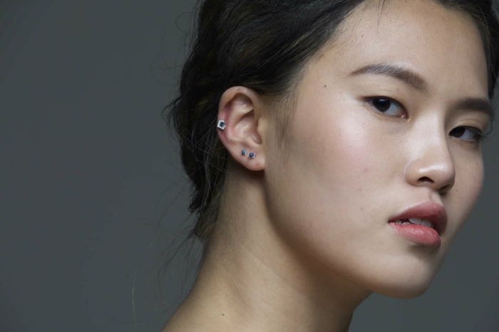 woman with black hair in a low updo, how much is a cartilage piercing, wearing earrings with blue rhinestones