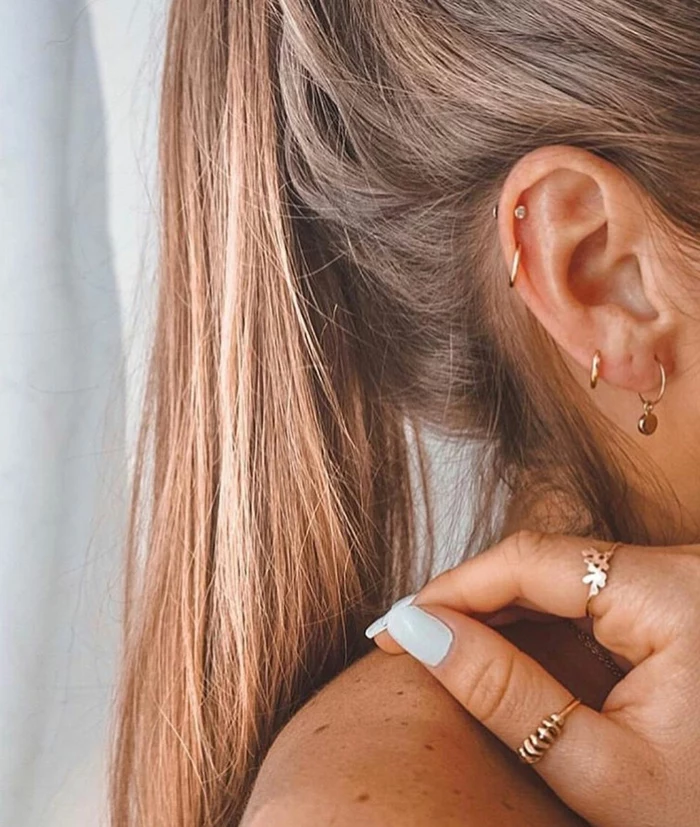 how to clean cartilage piercing, woman with blonde hair in a ponytail, wearing multiple different gold earrings