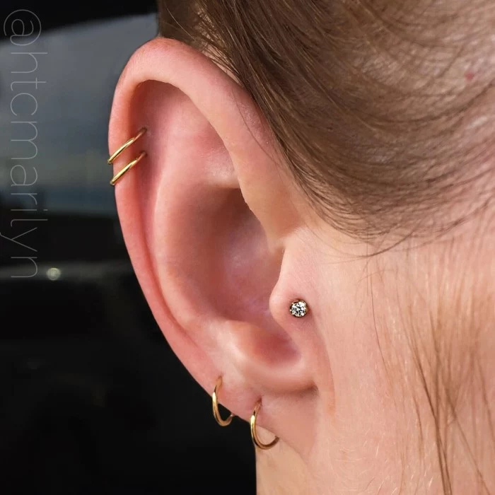 woman with brown hair, how to clean cartilage piercing, four gold ring earrings, one stud earring with rhinestone