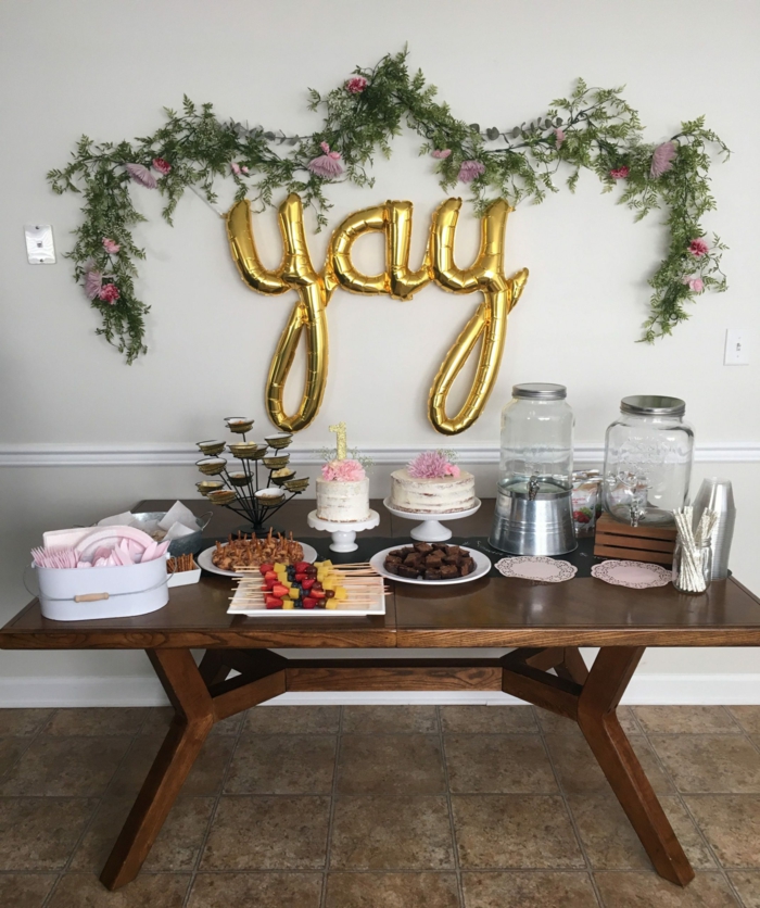 wooden table in front of white wall, different desserts placed on it, 80th birthday color, gold yay balloon on the wall