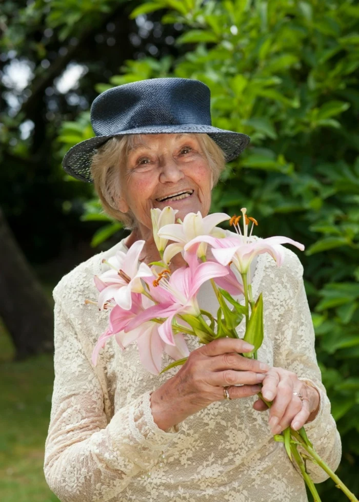 old lady with blonde hair, wearing white lace dress with long sleeves, 80th birthday color, holding a flower bouquet