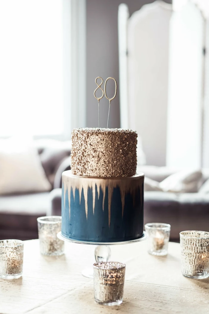 80th birthday ideas for dad, two tier cake, covered with blue and gold fondant, placed in the middle of table