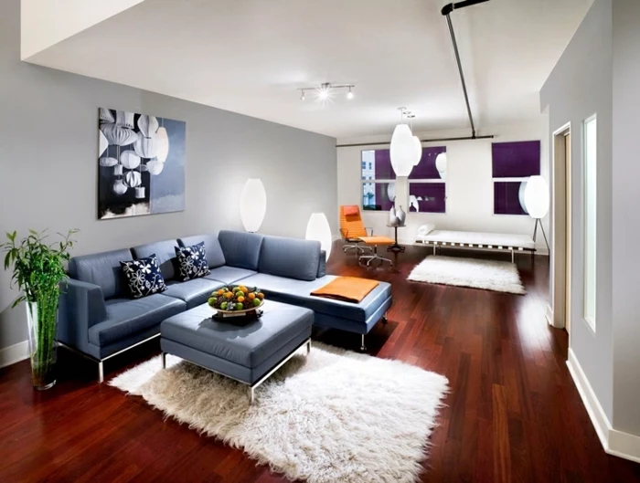 dark wooden floor, how to decorate your living room, blue leather corner sofa, blue leather ottoman, white rug