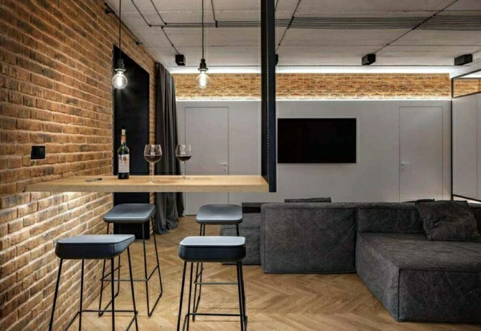 brick walls in industrial apartment, large grey corner sofa, wooden bar with black bar stools, modern living room