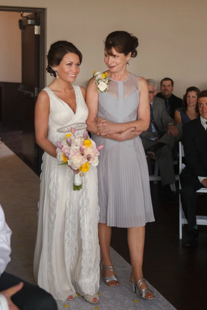 wedding entrance songs, bride being walked down the aisle by her mother, wearing a grey dress