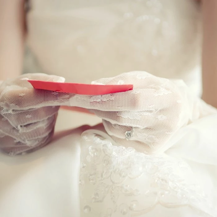bride wearing white lace gloves, holding a card in red envelope, wedding card message