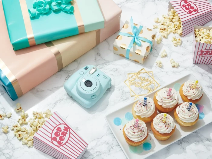 polaroid camera and popcorn, cupcakes and gifts, arranged on marble surface, birthday party themes