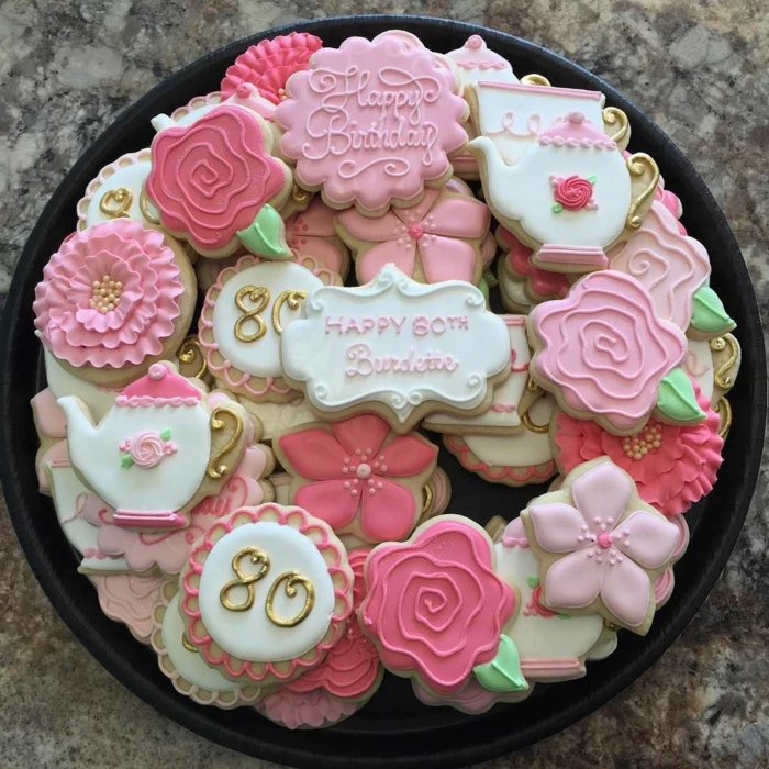 different cookies in the shapes of flowers and teapots, 80th birthday ideas for dad, arranged on black tray