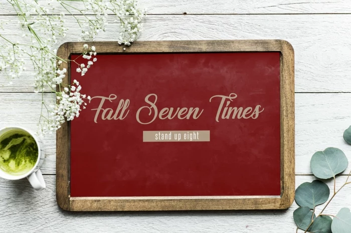 fall seven times stand up eight, written on red wooden board, tough times quotes, placed on white wooden surface
