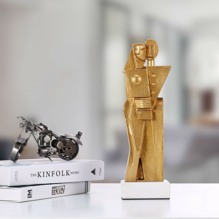 gold sculpture of man and woman hugging, traditional wedding anniversary gifts, placed on white surface, next to two books