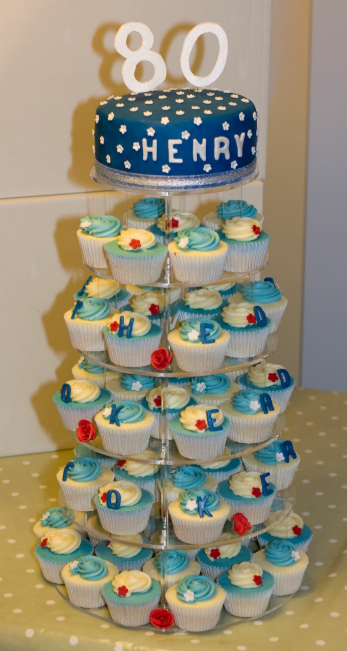 cake stand with lots of cupcakes arranged on it, one tier cake on top, 80th birthday ideas, blue fondant