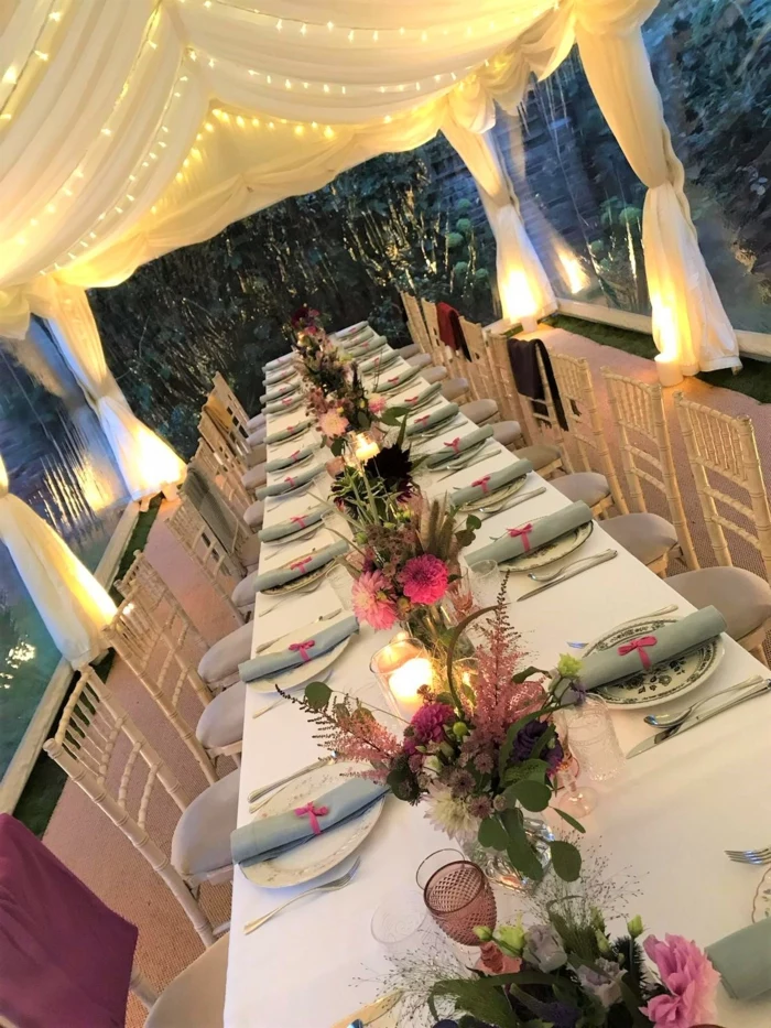 long table with plate settings, flower bouquets in the middle, tulle with fairy lights above it, 18th birthday party ideas
