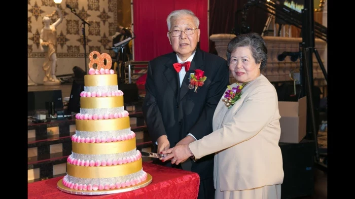 man and woman standing next to a table, 80th birthday party decorations, cutting into five tier cake