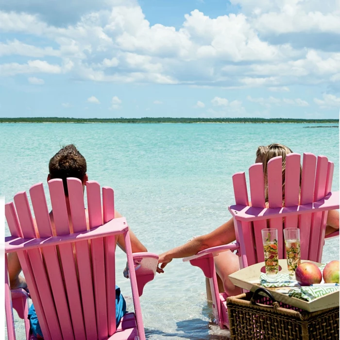 man and woman sitting on pink chairs at the beach, wedding anniversary gifts, holding hands