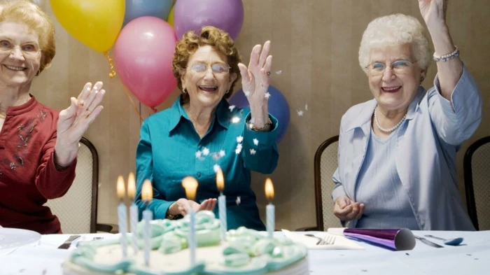three women smiling, sitting next to a table, 80th birthday, throwing confetti in the air