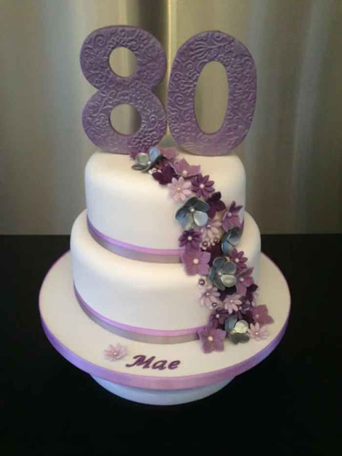 two tier cake, covered with white fondant, 80th birthday party favors, decorated with purple flowers