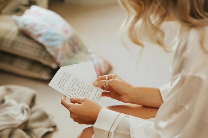 woman with blonde wavy hair, wearing white silk robe, reading a card, congratulations on your wedding