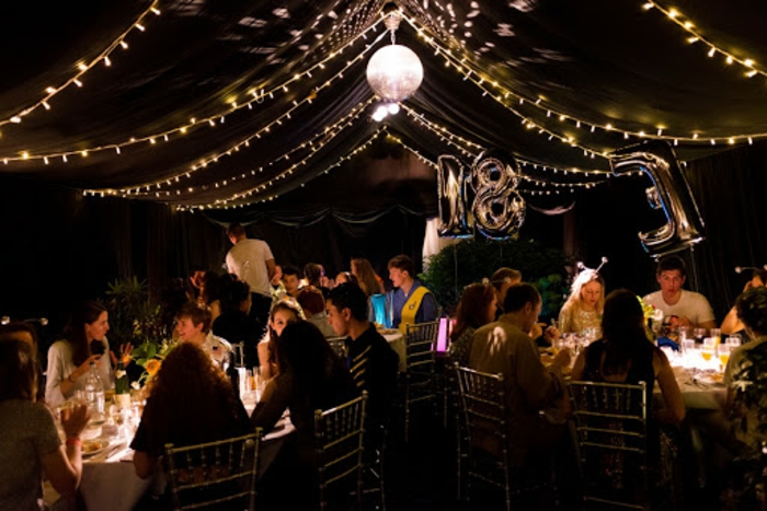 people sitting around round tables, 18th birthday ideas for boys, tulle and fairy lights hanging from the ceiling