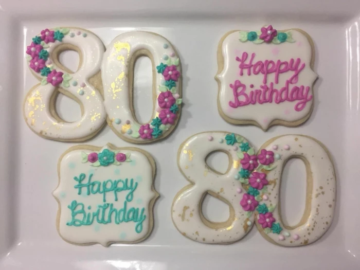 four cookies, two in the shape of number 80, 80th birthday party favors, decorated with purple flowers