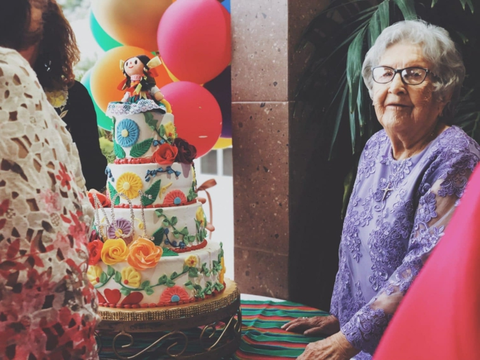 old lady wearing purple lace dress, 80th birthday, four tier cake on the table, decorated with flowers