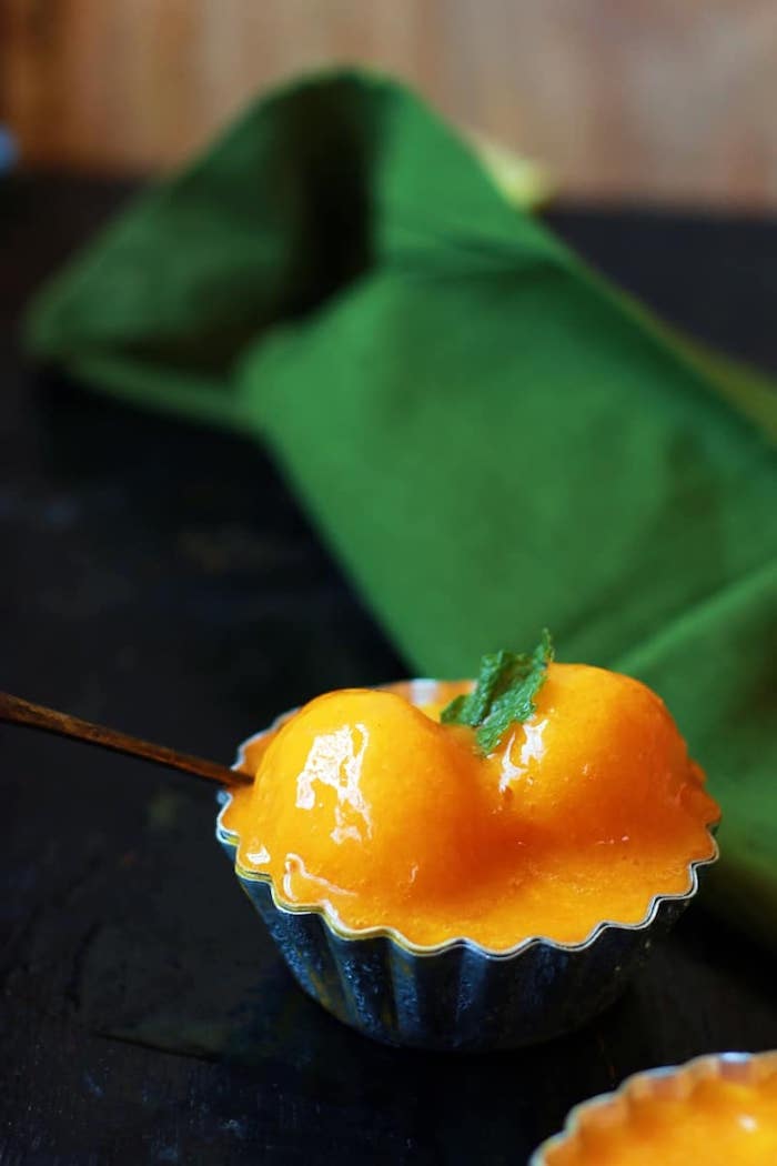 best summer desserts two scoops of mango sorbet slightly melted inside metal cupcake holder mini mint leaf on top