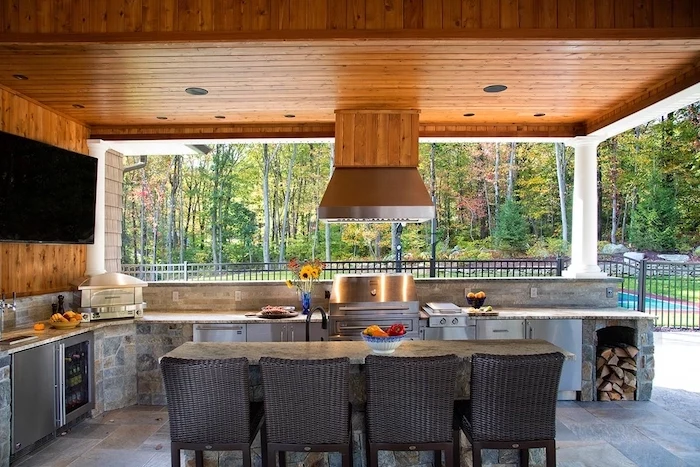 black chairs around table made of stone modern outdoor kitchen made of stone with grill fridge and cabinets wooden ceiling