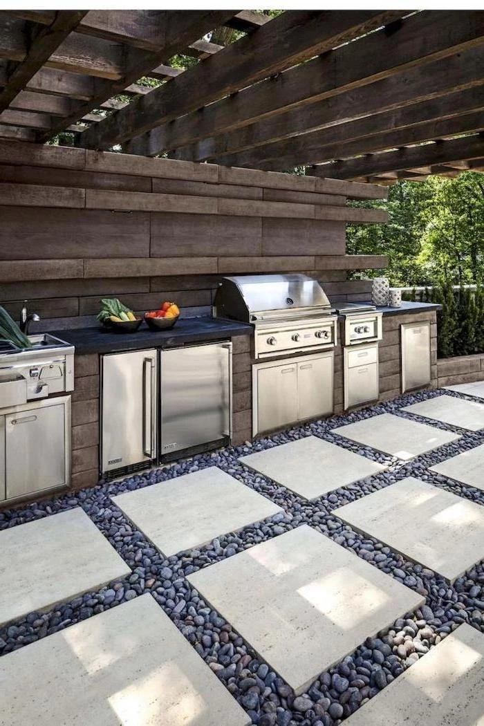 black countertop metal sink cabinets fridge grill covered outdoor kitchen stone tiles on the floor surrounded by small stones
