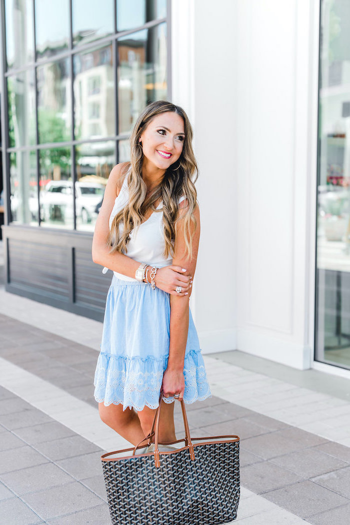 blonde woman with long wavy hair wearing blue lacy skirt with white top shorts summer outfits carrying black bag