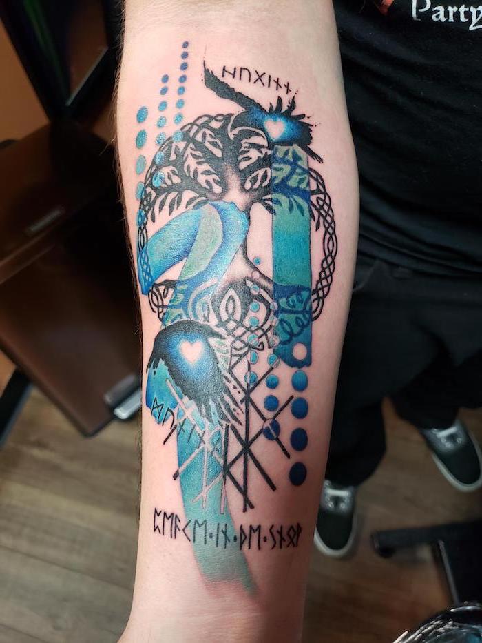 blue and black tree of life forearm tattoo polka tattoo style on man wearing black t shirt jeans