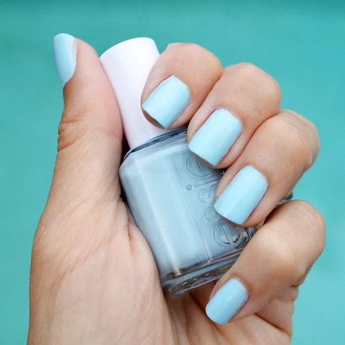 light blue nail polish, short square nails, hand holding a nail polish bottle, turquoise background