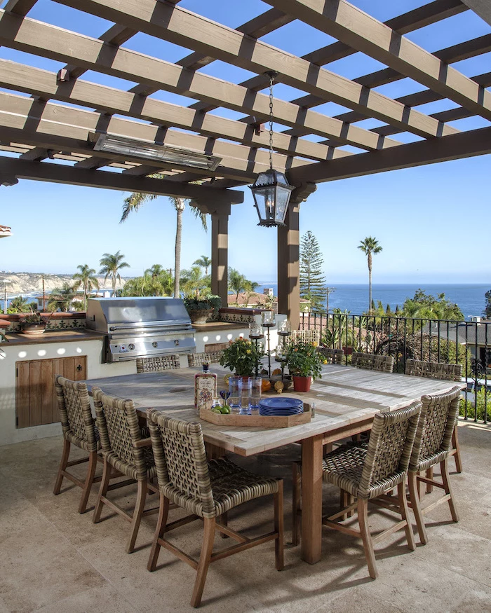 blue plates on large wooden table with chairs patio overlooking the sea modern outdoor kitchen wooden cabinets under the grill