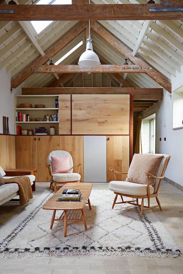 exposed wooden beams on white ceiling, farmhouse decor, bookshelf room separator, white armchairs and sofa