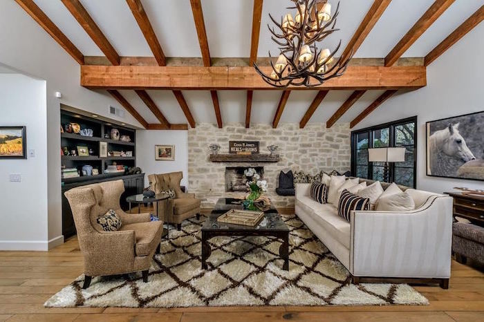 exposed wooden beams on white ceiling, modern farmhouse decor, white sofa and brown armchairs, white carpet on wooden floor