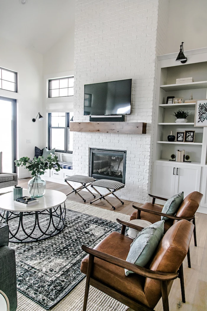 white brick wall with fireplace, farmhouse decor ideas, brown leather armchairs, white and black metal coffee table